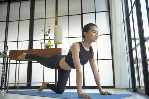 Asian woman in sportswear doing yoga on yoga mat in living room