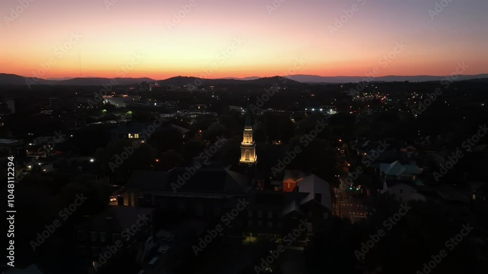 Aerial orbit shot of lighting church in dark american city after golden sunset. Dusk scene in small town with clear sky and mountain range silhouette. Wide shot. Aerial orbit shot of lighting church in dark american city after golden sunset. Dusk scene in small town with clear sky and mountain range silhouette. Wide shot.
