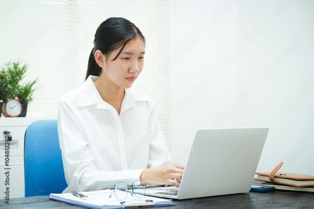 An Asian businesswoman smiles confidently while working at her desk in the office. She diligently analyzes financial data on her laptop, showcasing her expertise and commitment as an accountant An Asian businesswoman smiles confidently while working at her desk in the office. She diligently analyzes financial data on her laptop, showcasing her expertise and commitment as an accountant