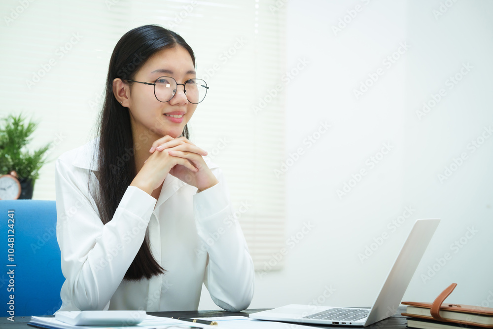 An Asian businesswoman smiles confidently while working at her desk in the office. She diligently analyzes financial data on her laptop, showcasing her expertise and commitment as an accountant An Asian businesswoman smiles confidently while working at her desk in the office. She diligently analyzes financial data on her laptop, showcasing her expertise and commitment as an accountant
