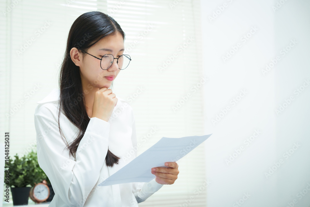 An Asian businesswoman smiles confidently while working at her desk in the office. She diligently analyzes financial data on her laptop, showcasing her expertise and commitment as an accountant An Asian businesswoman smiles confidently while working at her desk in the office. She diligently analyzes financial data on her laptop, showcasing her expertise and commitment as an accountant