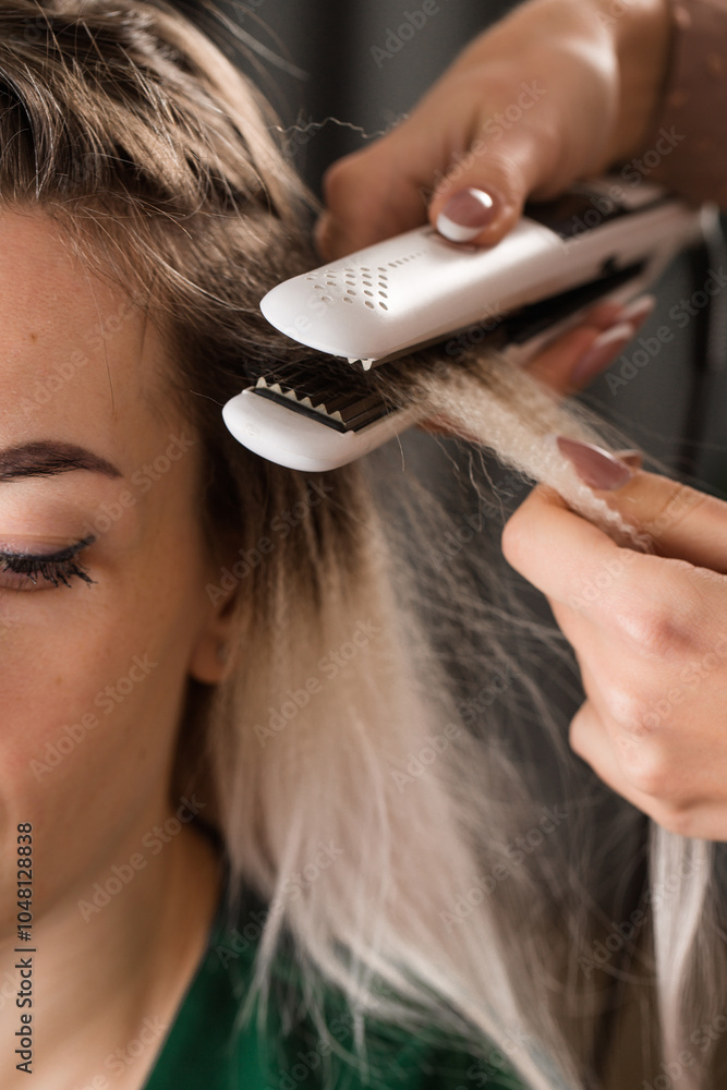 Fototapeta premium A stylist uses a curling iron to add volume