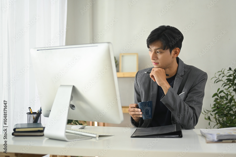 Focused young businessman analyzing data while drinking coffee at workplace Focused young businessman analyzing data while drinking coffee at workplace