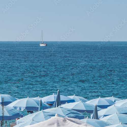 white and blue chairs on the beach and a white yacht in the see
