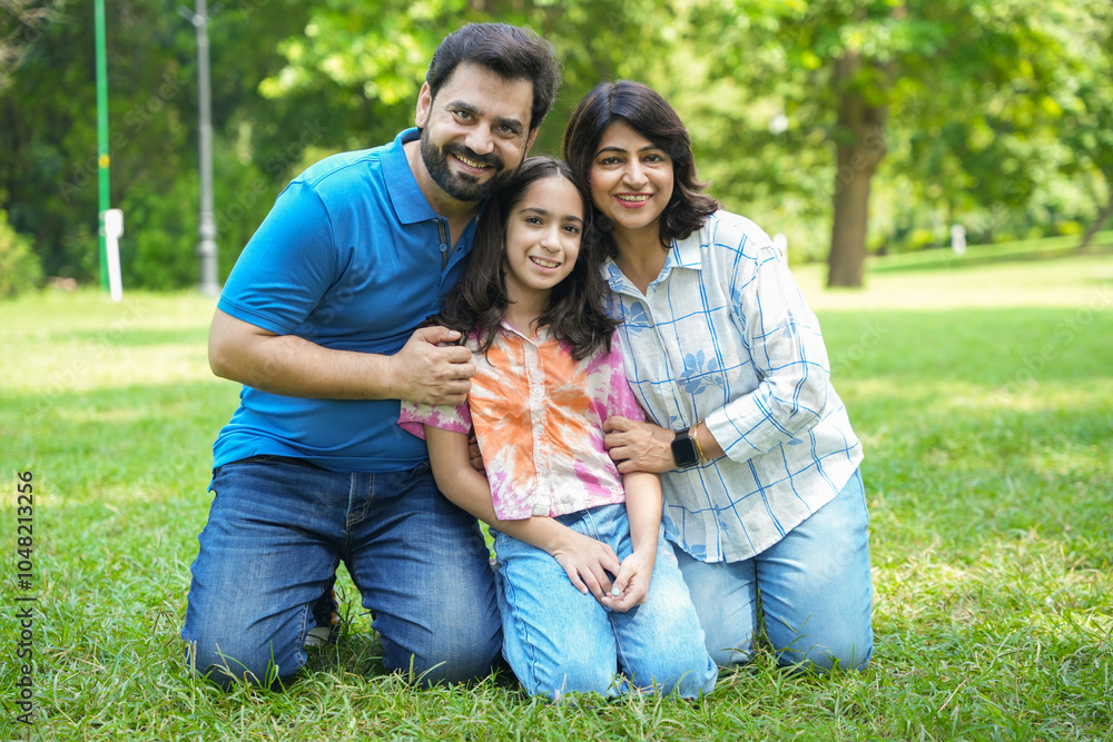 happy Indian family sitting in summer park enjoying time together. couple enjoying vacation with kid in garden while looking at camera. happy Indian family sitting in summer park enjoying time together. couple enjoying vacation with kid in garden while looking at camera.