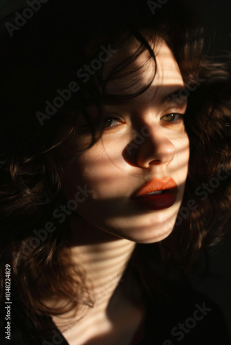 Portrait of a young woman with curly hair and a contemplative expression, illuminated by dramatic shadows and soft light creating a moody atmosphere.