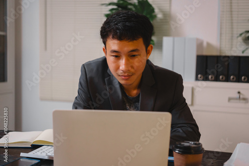 A businessman works late at his desk, focused on his laptop while talking online. He checks important financial documents, demonstrating dedication and diligence as he manages his overtime tasks