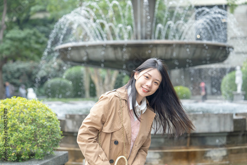 A long-haired Taiwanese woman in her 20s wearing a beige trench coat spends her winter afternoon around a fountain in a park in Xinyi District, Taipei, Taiwan, on January 30, 2024. photo