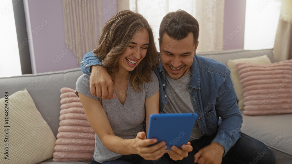 Smiling man and woman sitting together on a cozy couch in their living room, enjoying a moment while looking at a tablet Smiling man and woman sitting together on a cozy couch in their living room, enjoying a moment while looking at a tablet