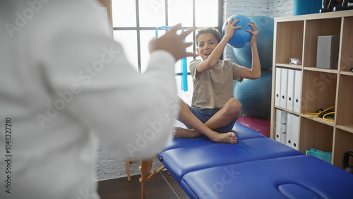 Fotografie A woman therapist guides a boy with exercise ball during pediatric physiotherapy session in clinic