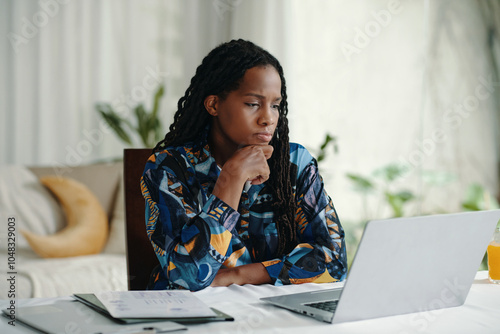 Canvas Print Woman thinking while sitting at a desk with an open laptop and documents near wi