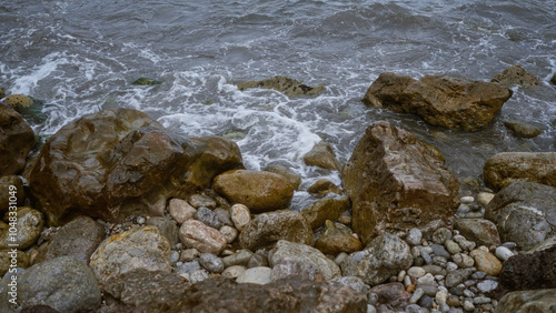 Rocky shoreline with waves hitting the rocks at a beach, showcasing natural coastal scenery with wet stones and turbulent water, the elements highlighting rugged beauty and natural textures.