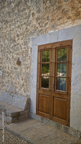 Stone facade with wooden door and stone bench in mallorca, spain showcases rustic mediterranean architecture and outdoor charm on a sunny day.