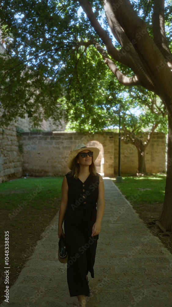 Young woman in a black dress and sunhat walking outdoors in palma mallorca spain surrounded by trees and old stone walls Young woman in a black dress and sunhat walking outdoors in palma mallorca spain surrounded by trees and old stone walls