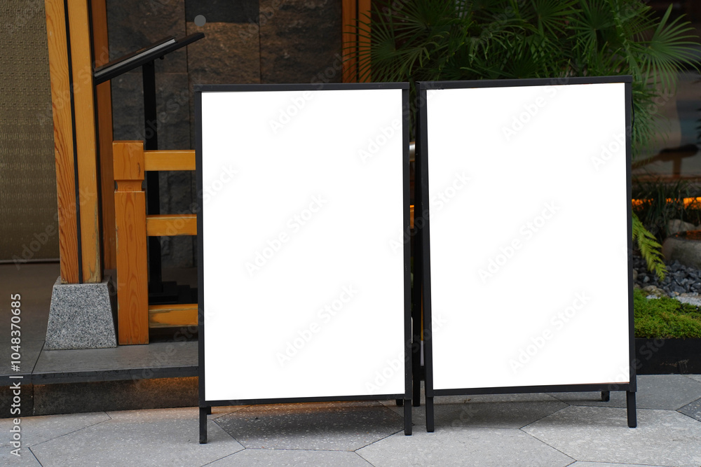 Blank white outdoor advertising stand sandwich board mock up template. Clear street signage board placed by an outdoor dinning area of a restaurant.