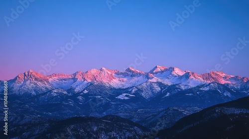 A clear twilight sky over snow-capped mountains, with the last rays of sunlight reflecting on the peaks and a deep blue sky above