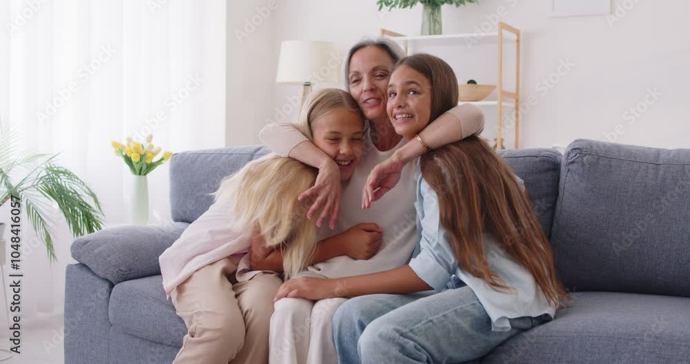 Happy smiling mother sitting on sofa, hugging her two loving preteen daughters and cuddling them up to yourself. Joyful family sharing tender and warm moment of love and affection in their cozy home. Happy smiling mother sitting on sofa, hugging her two loving preteen daughters and cuddling them up to yourself. Joyful family sharing tender and warm moment of love and affection in their cozy home.