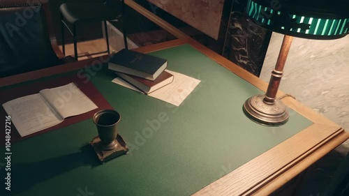 An old-fashioned desk with a lamp, books, a rotary phone, a folder with documents and pens for writing. A leather chair is nearby. Shot in motion