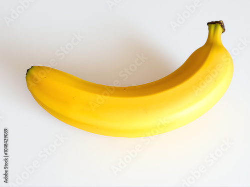 A ripe yellow banana resting on a clean white surface with natural lighting highlighting its smooth texture photo