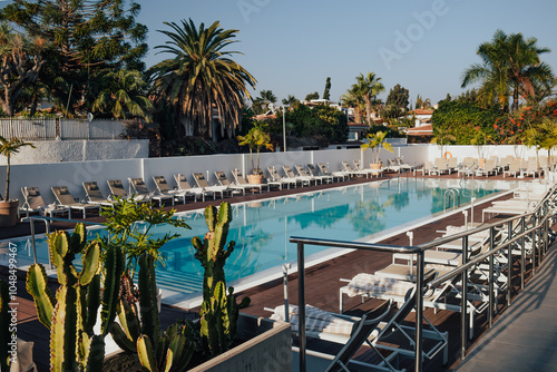 Empty swimming pool with sunbed in resort hotel. Vacation leisure. Blue water and reflection of palms. Pastel lounge chairs and close beach umbrellas. Tourism and advertising concept. Morning