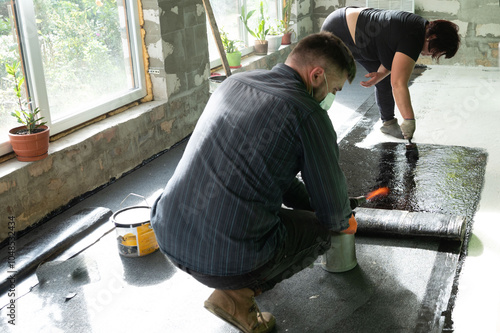 A man and a woman are engaged in waterproofing the floor in the house.