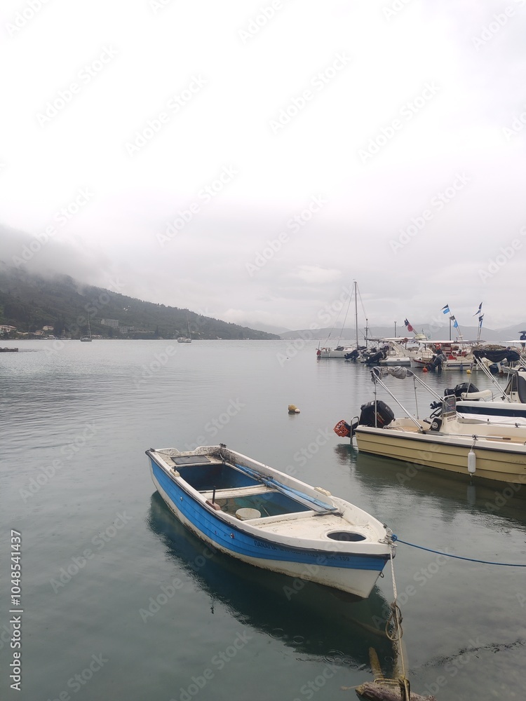 Fototapeta premium Small boats in a misty harbour with mountains in the background