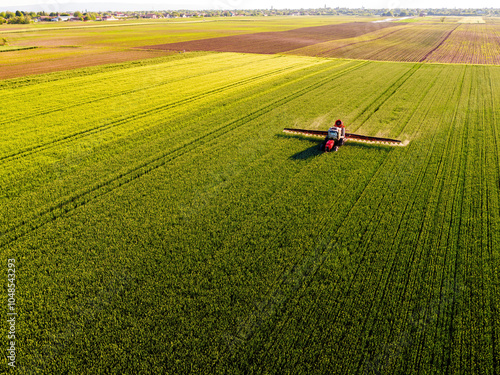 Canvastavla Drone shot of a tractor with sprayer in action on a vibrant green wheat farmland