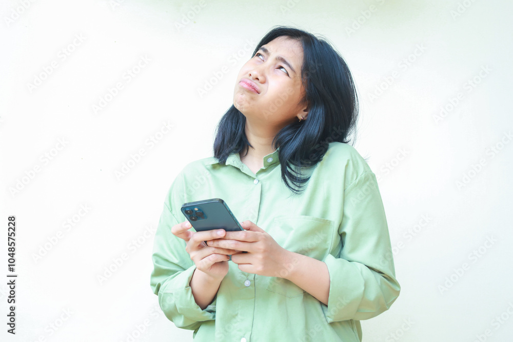portrait of unhappy asian woman wearing over size green clothes looking above showing sad gloomy face expression confused using smartphone apps and online shopping isolated on white background portrait of unhappy asian woman wearing over size green clothes looking above showing sad gloomy face expression confused using smartphone apps and online shopping isolated on white background