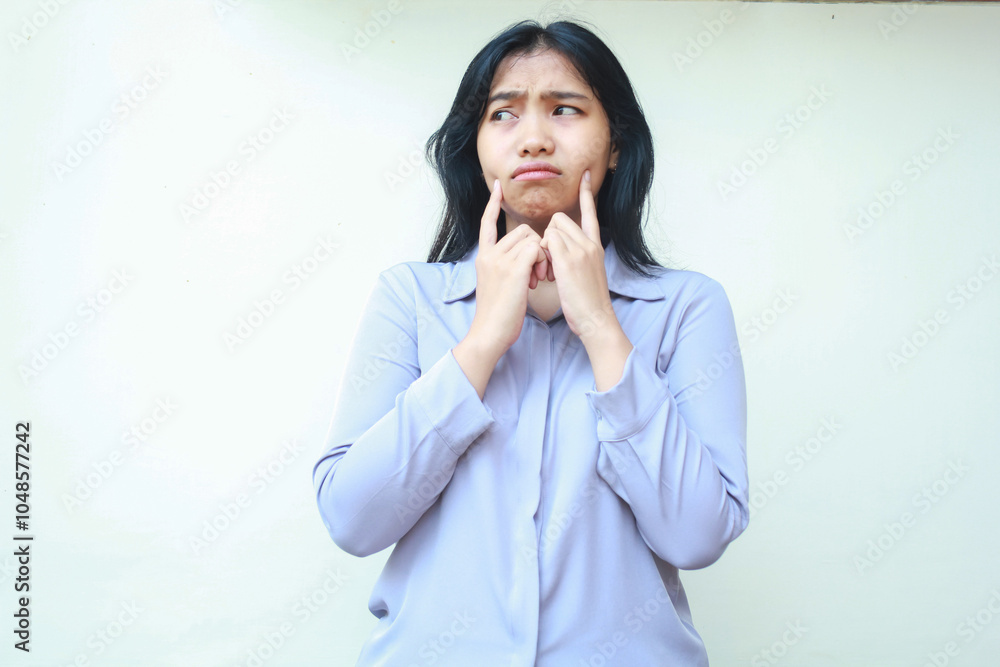sad worried asian young woman looking away with thoughtful expression and thouching her cheek with forefinger isolated over white background