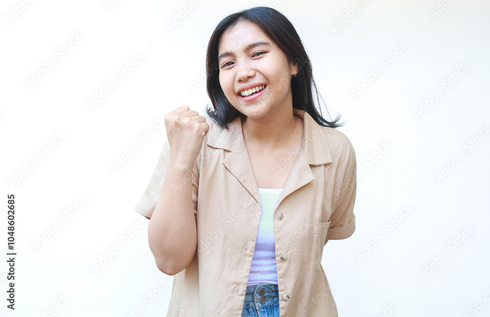 happy asian woman celebrate victory with raised fist wearing casual brown clothes isolated on white background happy asian woman celebrate victory with raised fist wearing casual brown clothes isolated on white background
