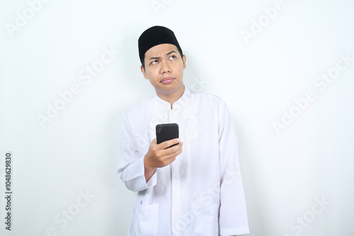 confused muslim asian man looking above think about something with holding mobile phone isolated on white background