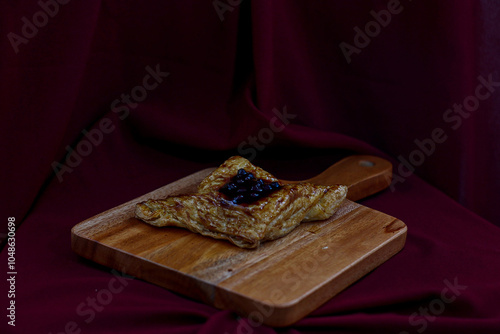 DRY BREAD WITH BLUEBERRY JAM ON TOP AND SERVED ON A WOODEN TRAY.