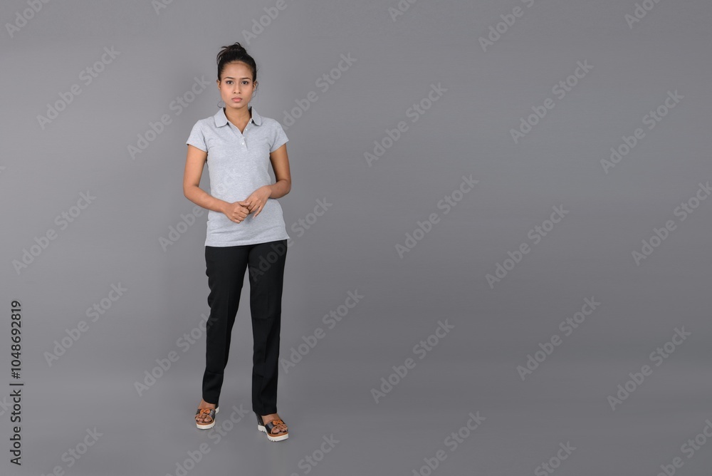 Young woman wearing grey polo t-shirt, black trousers and heels posing with cheerful expressions against grey background. Young woman wearing grey polo t-shirt, black trousers and heels posing with cheerful expressions against grey background.