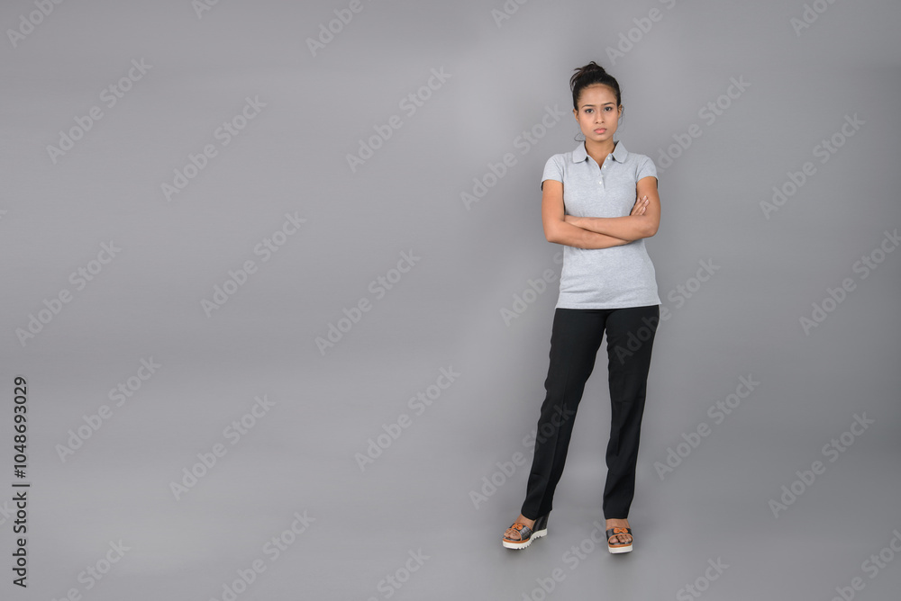 Young woman wearing grey polo t-shirt, black trousers and heels posing with cheerful expressions against grey background.