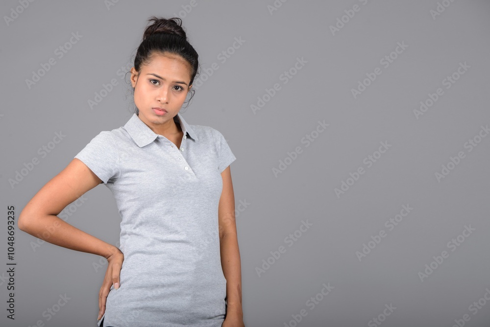 Young woman wearing grey polo t-shirt, black trousers and heels posing with cheerful expressions against grey background. Young woman wearing grey polo t-shirt, black trousers and heels posing with cheerful expressions against grey background.