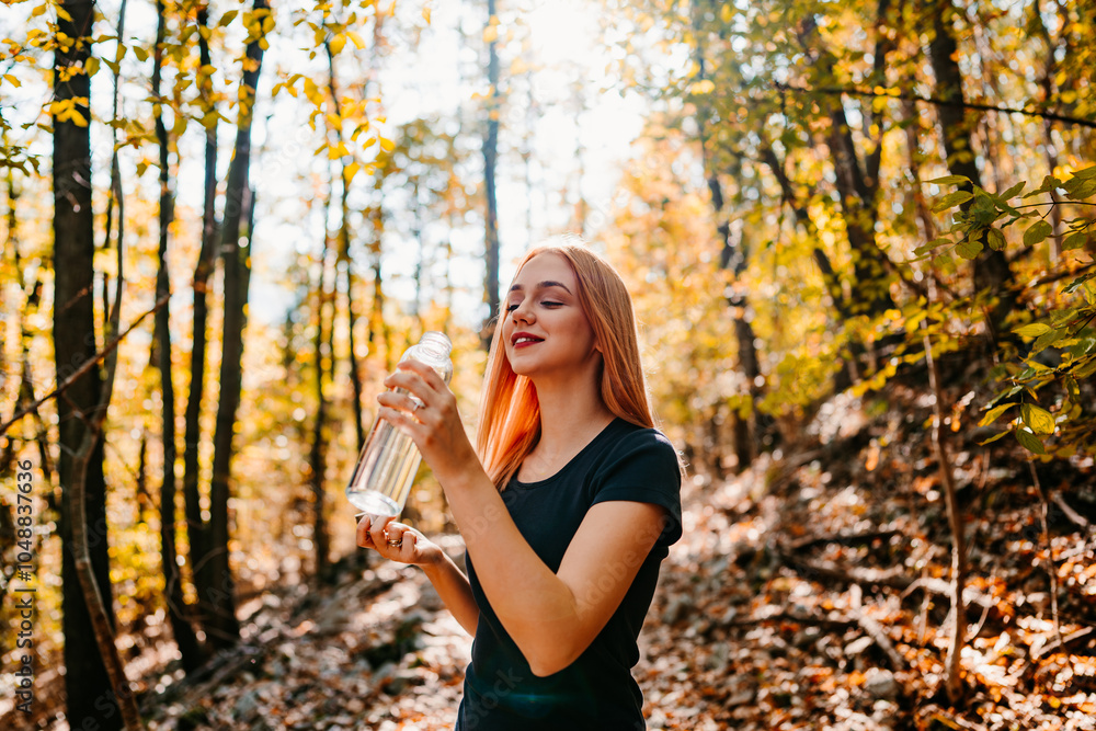 Beautiful young redhead woman walking and jogging in the woods with bottle of drinking water. Healthy lifestyle and sport in nature concept. Beautiful young redhead woman walking and jogging in the woods with bottle of drinking water. Healthy lifestyle and sport in nature concept.