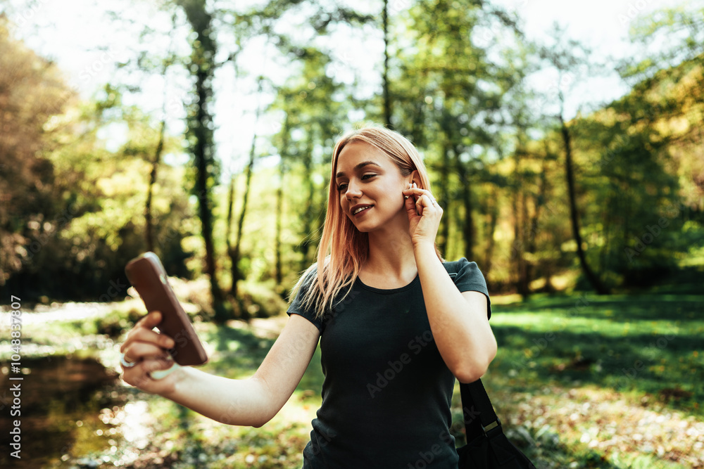 Beautiful redhead sporty woman jogging and walking in the woods. She is using smart phone and wireless earbuds for music listening and video calls with her friends. Beautiful redhead sporty woman jogging and walking in the woods. She is using smart phone and wireless earbuds for music listening and video calls with her friends.