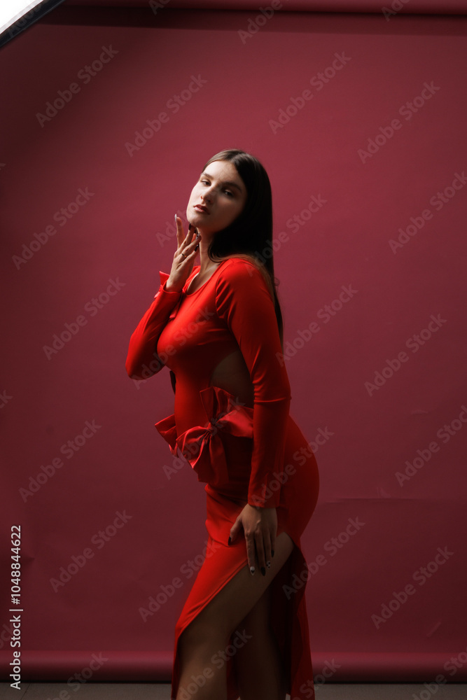 Obraz premium Beautiful young pregnant brunette girl. A woman waiting for a baby in a red dress with bows, on red background, in the studio.