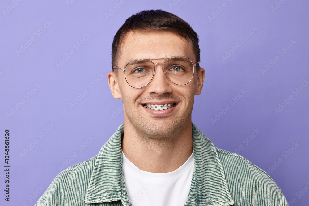 Fototapeta premium Smiling man with dental braces on violet background