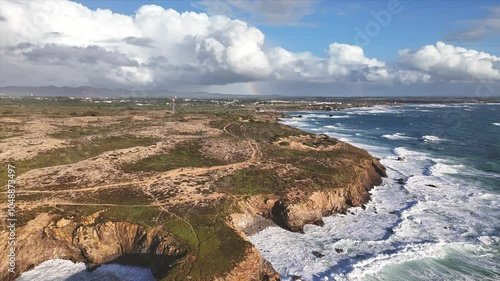 Aerial view of the Portuguese coastline on the west of Alentejo region. Giant ocean surf in the foreground and dramatic clouds and rainbow in the background