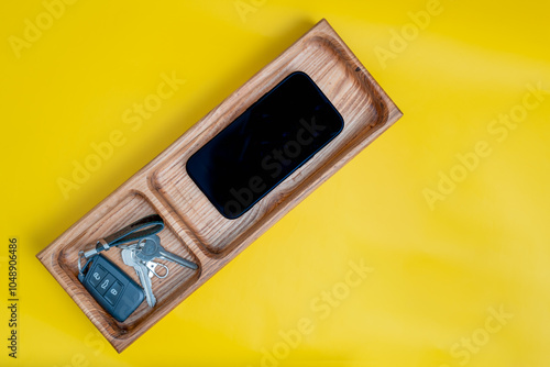 hardwood hand crafted catch all valet tray with cell phone and keys isolated on a yellow background photo