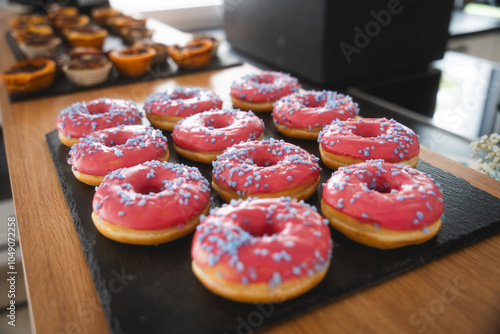 Donuts glazed with pink sugar and purple sprinkels served on a black slate plate, delicious bakery dessert, food photography photo