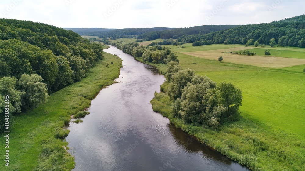 Fototapeta premium A serene river winding through lush greenery and fields, showcasing natural beauty.