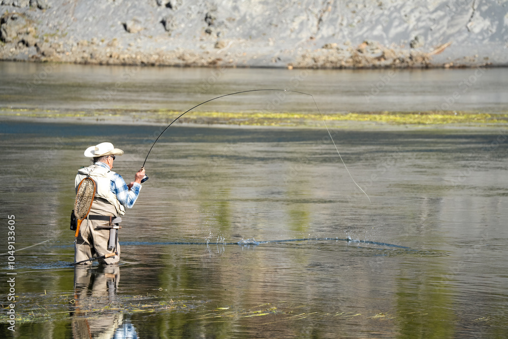 a fly fisherman in waders stood mid-river, using a two-handed rod to cast a fly line a fly fisherman in waders stood mid-river, using a two-handed rod to cast a fly line