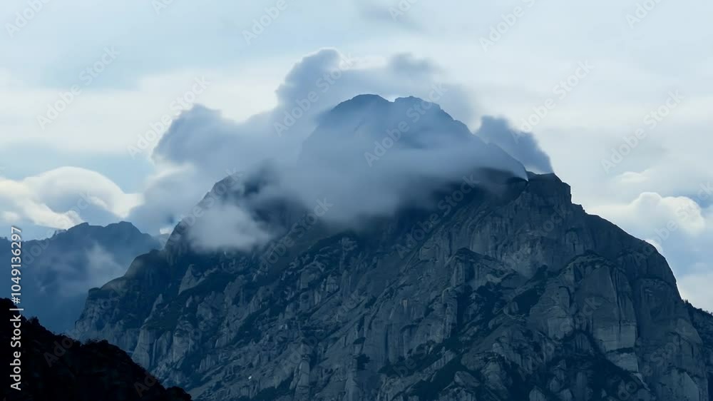 Dramatic view of a mountain peak with clouds swirling around it, as seen from a distance. Dramatic view of a mountain peak with clouds swirling around it, as seen from a distance.