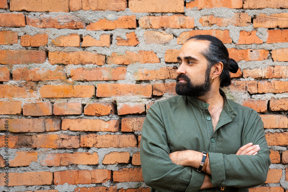 Obraz premium A dark-haired, bearded man of Dominican appearance in a green shirt against a brick red wall. The man near the wall looks away. Empty space for text. High quality photo
