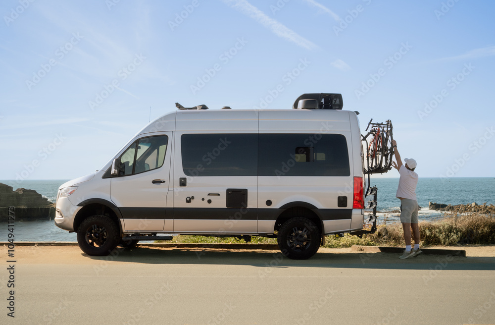 Naklejka premium Man taking down his bike from mobile home while parked at Asilomar Beach in Pacific Grove, California. Wide shot