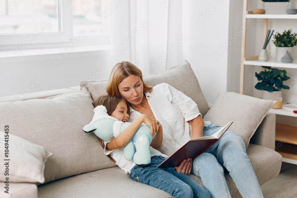 Woman reading a book to a little girl on a cozy couch in a warmly lit living room Woman reading a book to a little girl on a cozy couch in a warmly lit living room