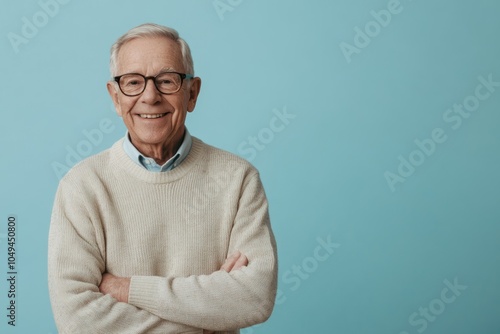 Elderly male presenter, smiling, in a casual sweater, in front of a solid light blue background with space for messaging