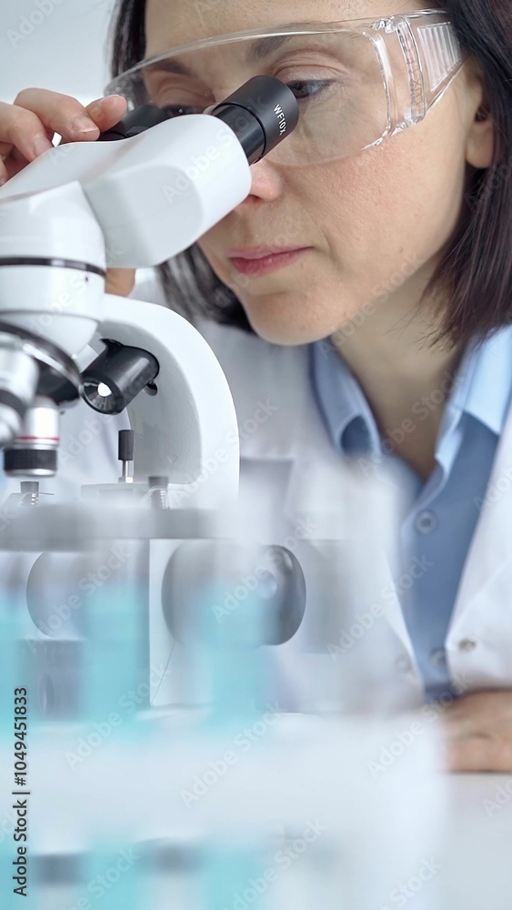 Female scientist using microscope in laboratory, portrait. Focus on a woman in lab goggles analyzing samples in a scientific setting Female scientist using microscope in laboratory, portrait. Focus on a woman in lab goggles analyzing samples in a scientific setting